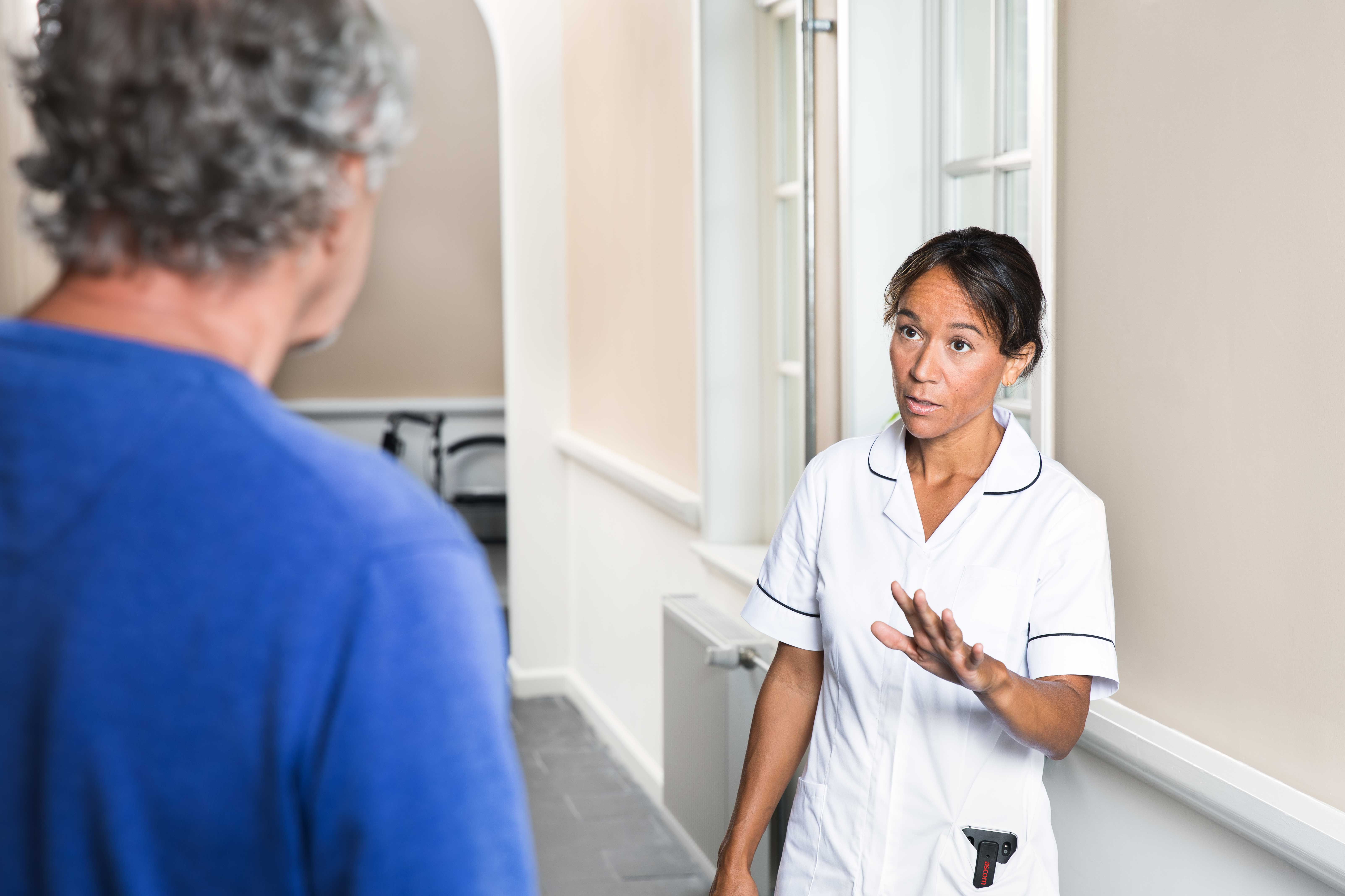 Caregiver in uniform signaling elderly resident to stop going towards her with device in her pocket